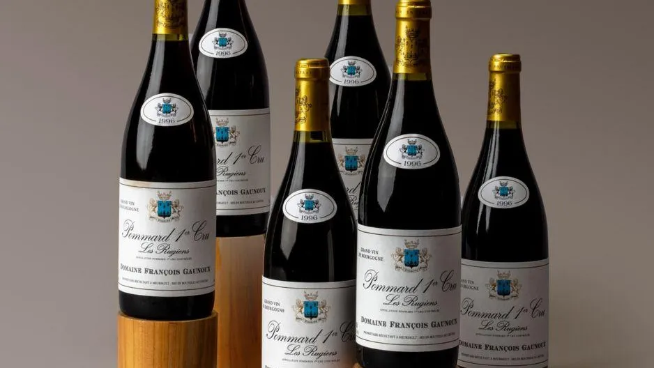 Six bouteilles de vin rouge avec étiquette "Pommard 1er Cru" posées sur des supports en bois