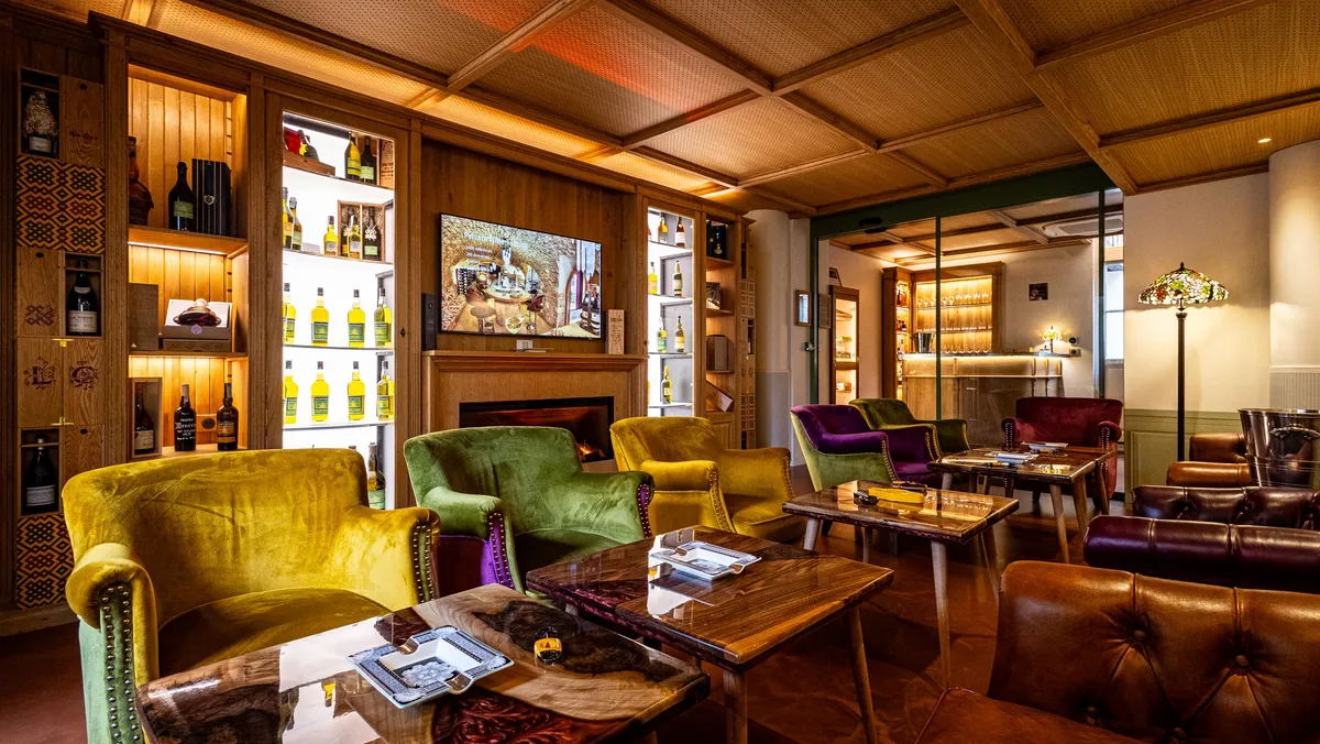 Un salon avec des fauteuils colorés, des tables basses et une cheminée, entouré d'étagères remplies de bouteilles d'alcool