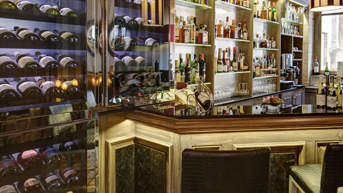 A bar with shelves stocked with wine and various spirits, glasses and bar accessories visible on the counter.