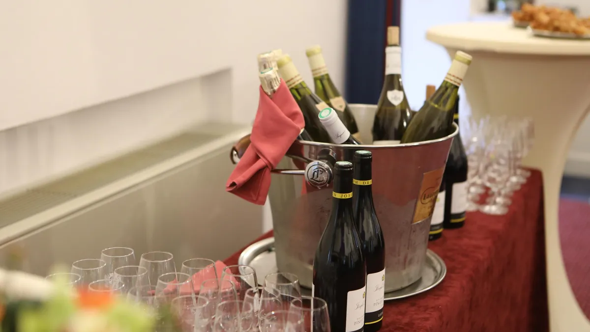 Un seau à glace contenant des bouteilles de vin avec un torchon rouge, entouré de verres à vin sur une table