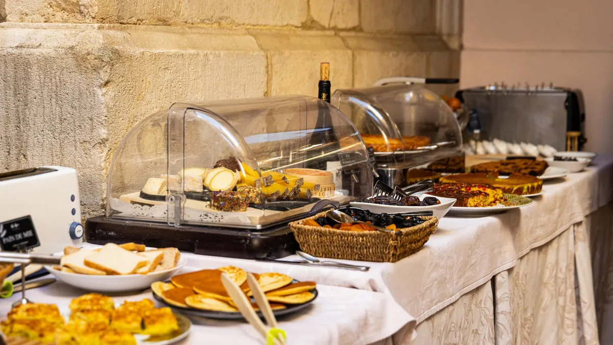 Un buffet de petit-déjeuner avec des plats couverts de cloches en verre, des assiettes de pain, des fruits et des boissons sur une table