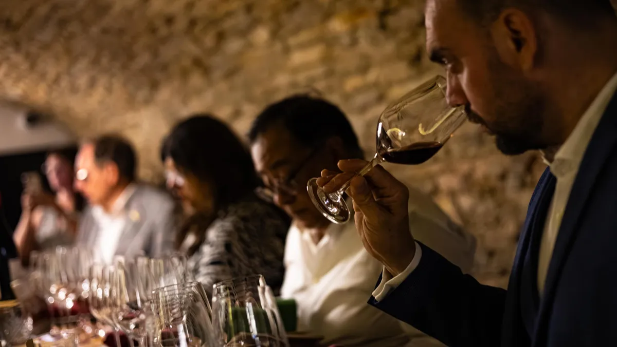 Several people sitting at a table with wine glasses, one of them smelling the contents of their glass.