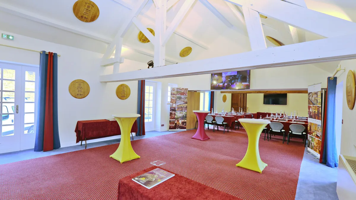 Reception room with yellow high tables, round tables and chairs, decorated with red curtains and wooden panels on the ceiling.
