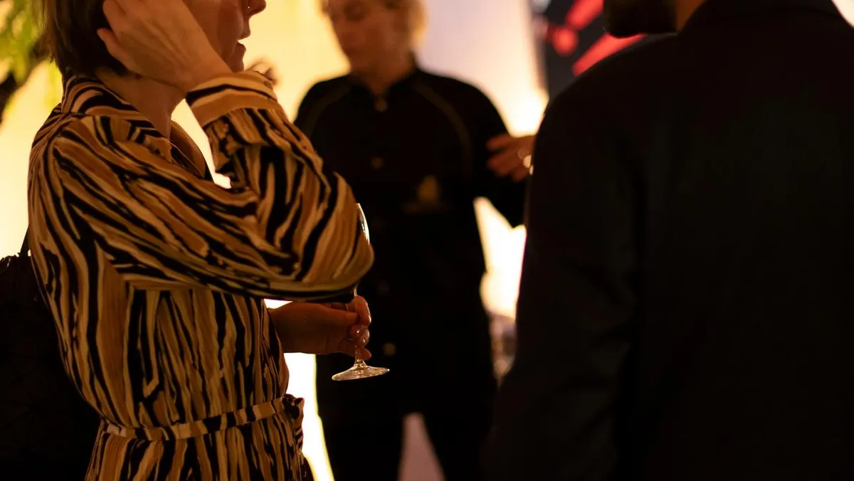 Deux personnes discutent dans un cadre extérieur, l'une tenant un verre de vin