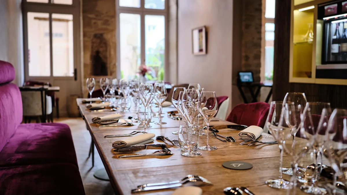 A long wooden table is set with wine glasses, cutlery, and napkins for a meal in an elegant restaurant.