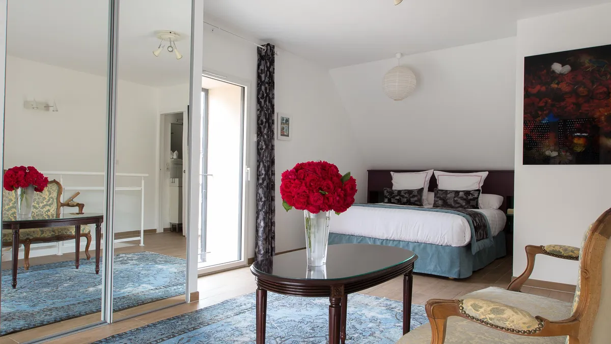 Chambre avec lit, table basse, chaises et miroir, décorée de fleurs rouges et de tapis bleu