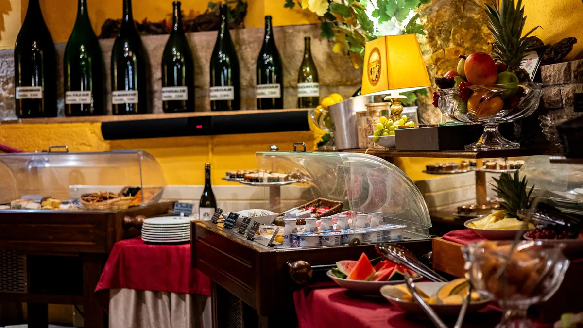 Un buffet de petit-déjeuner avec des plats couverts, des fruits, des boissons et des bouteilles de vin alignées sur une étagère