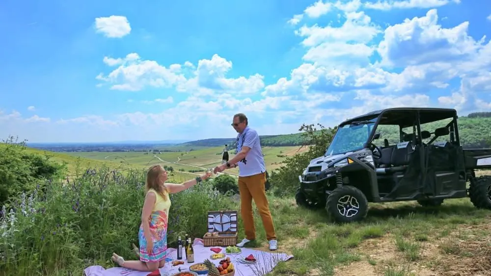 Un homme et une femme pique-niquent en plein air près d'un véhicule tout-terrain, avec une vue dégagée sur la campagne