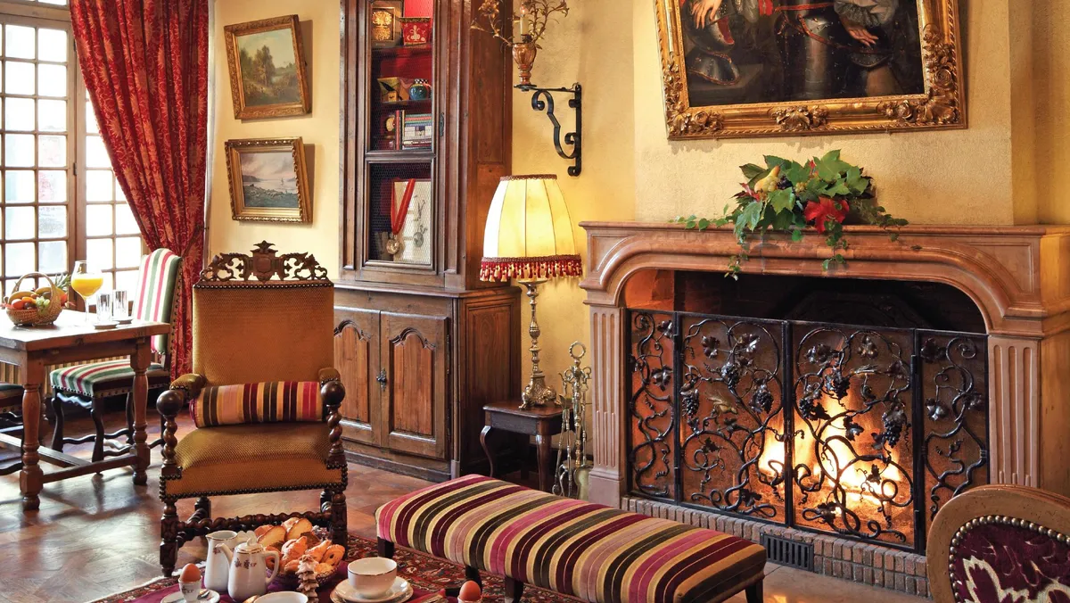 Salon avec cheminée, chandeliers, tableaux, meubles anciens et une table avec des tasses et des pâtisseries
