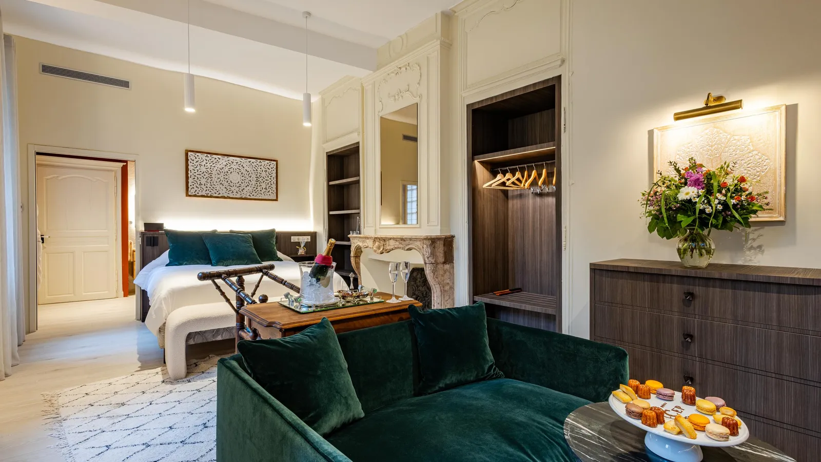 Chambre luxueuse avec canapé vert, table basse garnie de pâtisseries, lit blanc et dressing ouvert