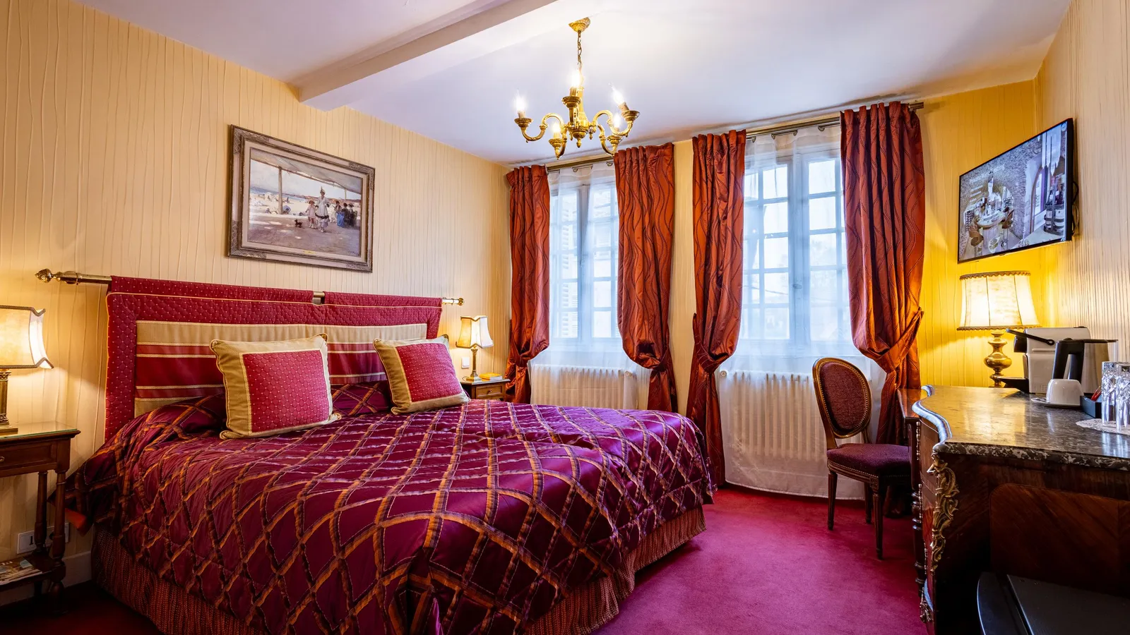 Chambre élégante avec un grand lit à baldaquin recouvert d'une couverture à motifs rouges et or, des tables de chevet avec lampes, des rideaux rouges, une fenêtre, un bureau et des œuvres d'art au mur