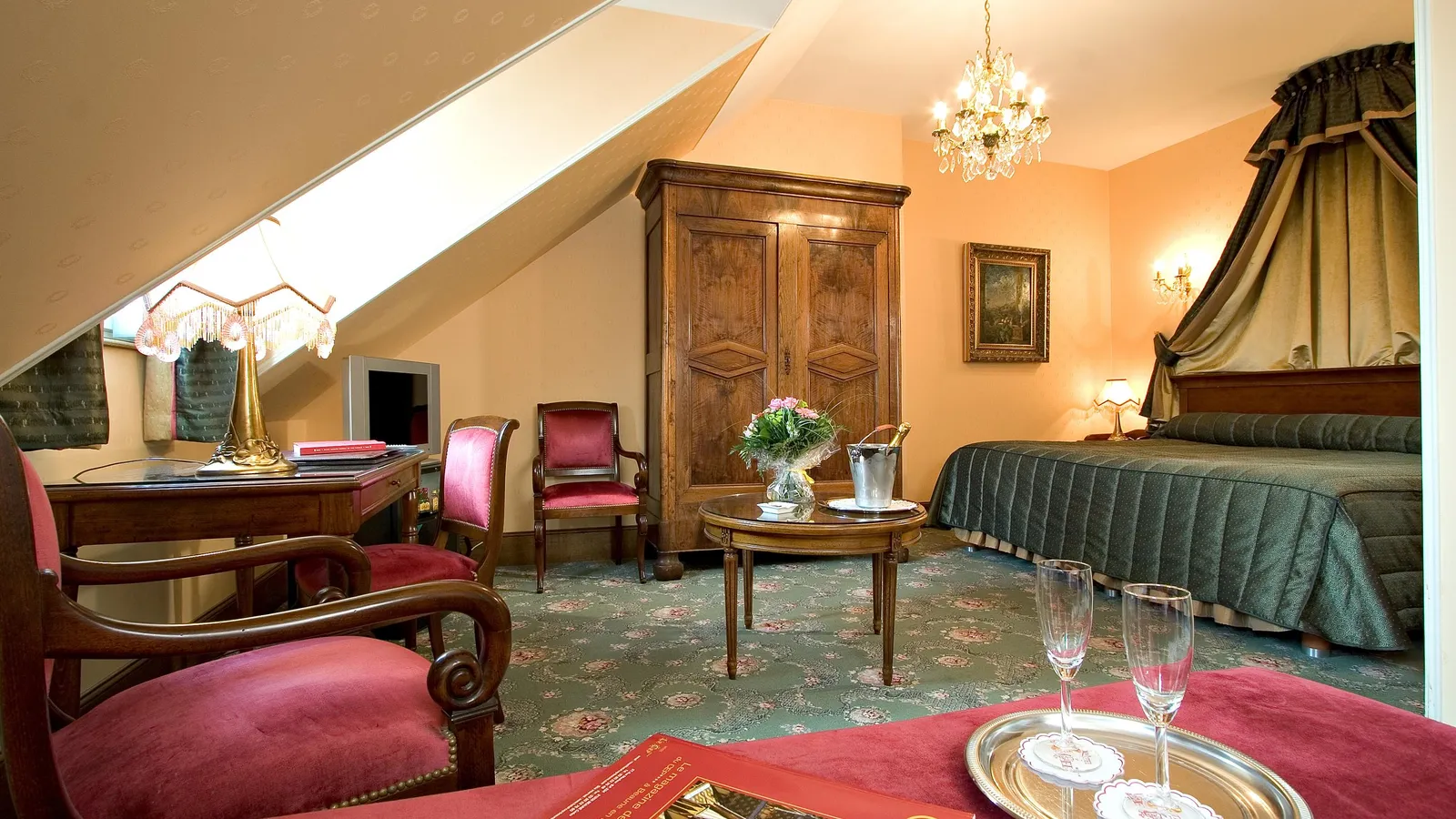 Elegant room with a four-poster bed, table with two champagne glasses, wooden wardrobe and floral decorations.