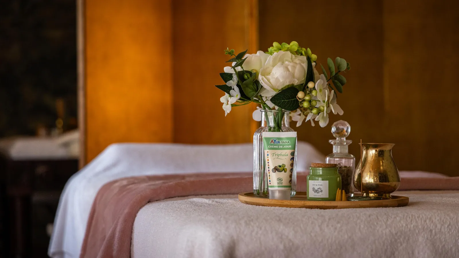 Un plateau avec des produits de soin, un vase de fleurs et une bougie posée sur une table recouverte d'une serviette
