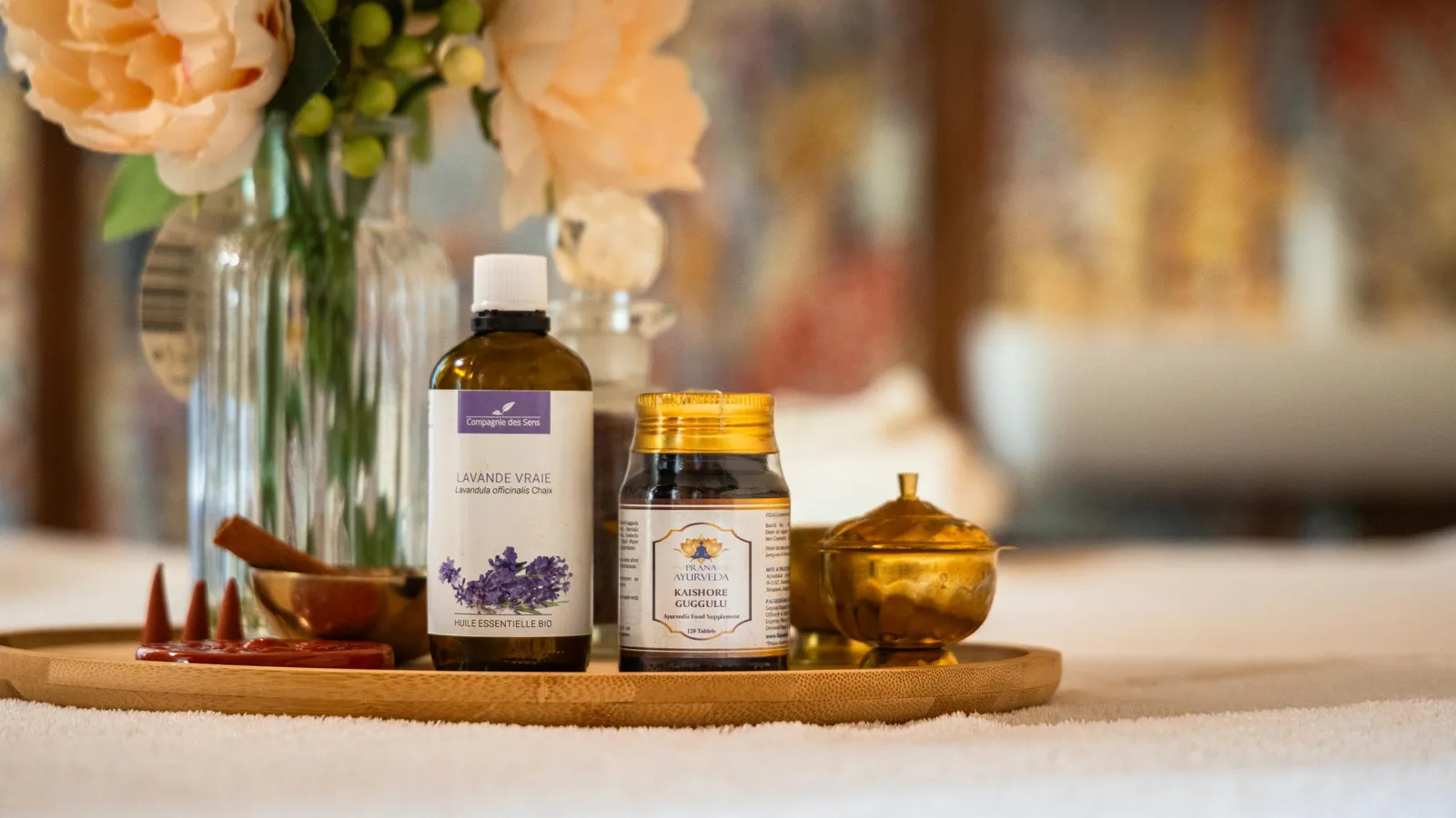 Bouteille d'huile essentielle de lavande, pot de guggulu et petit récipient doré posés sur un plateau en bois