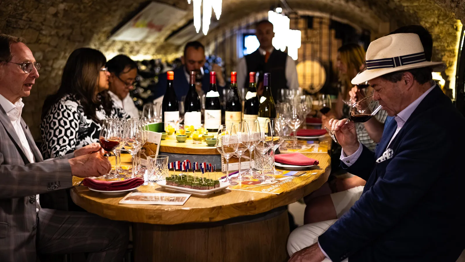 Un groupe de personnes déguste du vin autour d'une table garnie de verres et de bouteilles dans un cadre souterrain