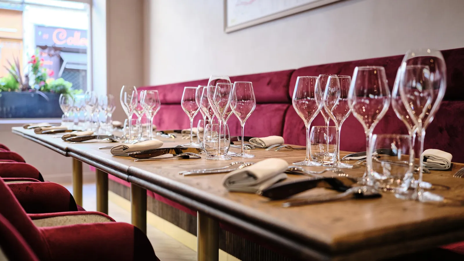 Une table de restaurant avec des verres à vin, des couverts et des serviettes sur une nappe, devant une banquette rouge
