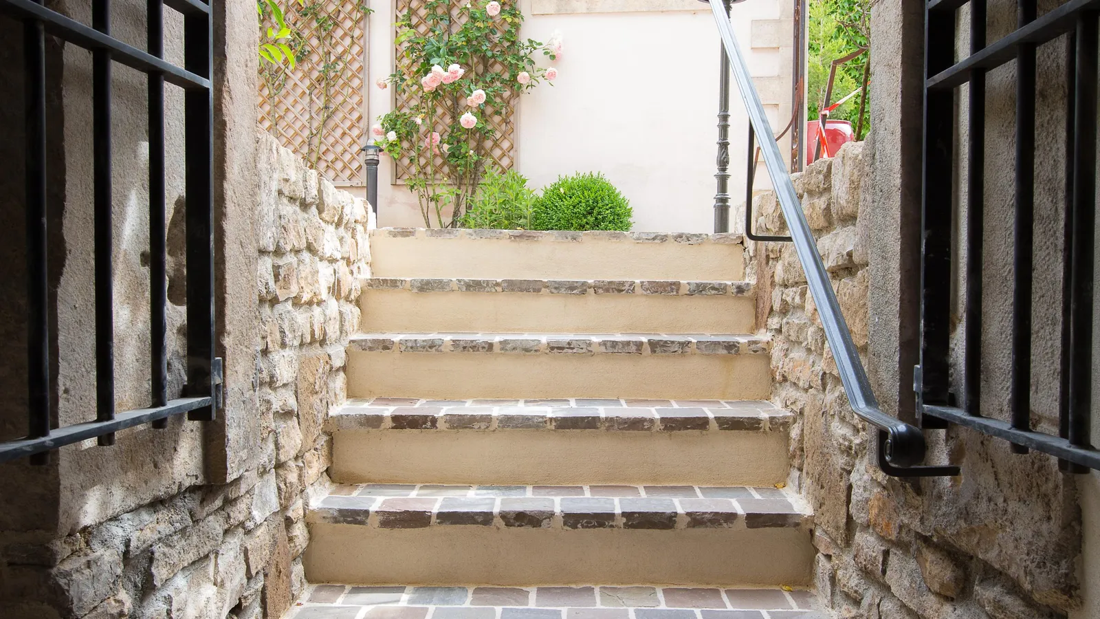 A stone staircase leads up to a garden with climbing roses and a building in the background.