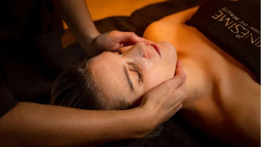 A person receives a facial and neck massage while lying on a massage table.