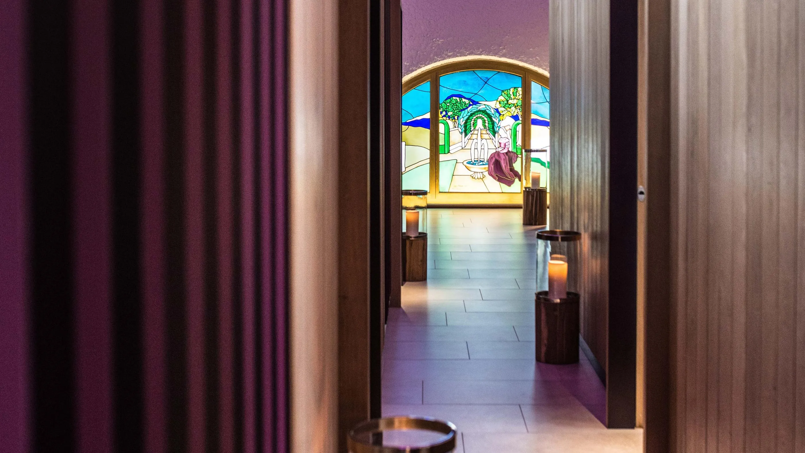View of a hallway leading to a room with colored stained glass and lit candles