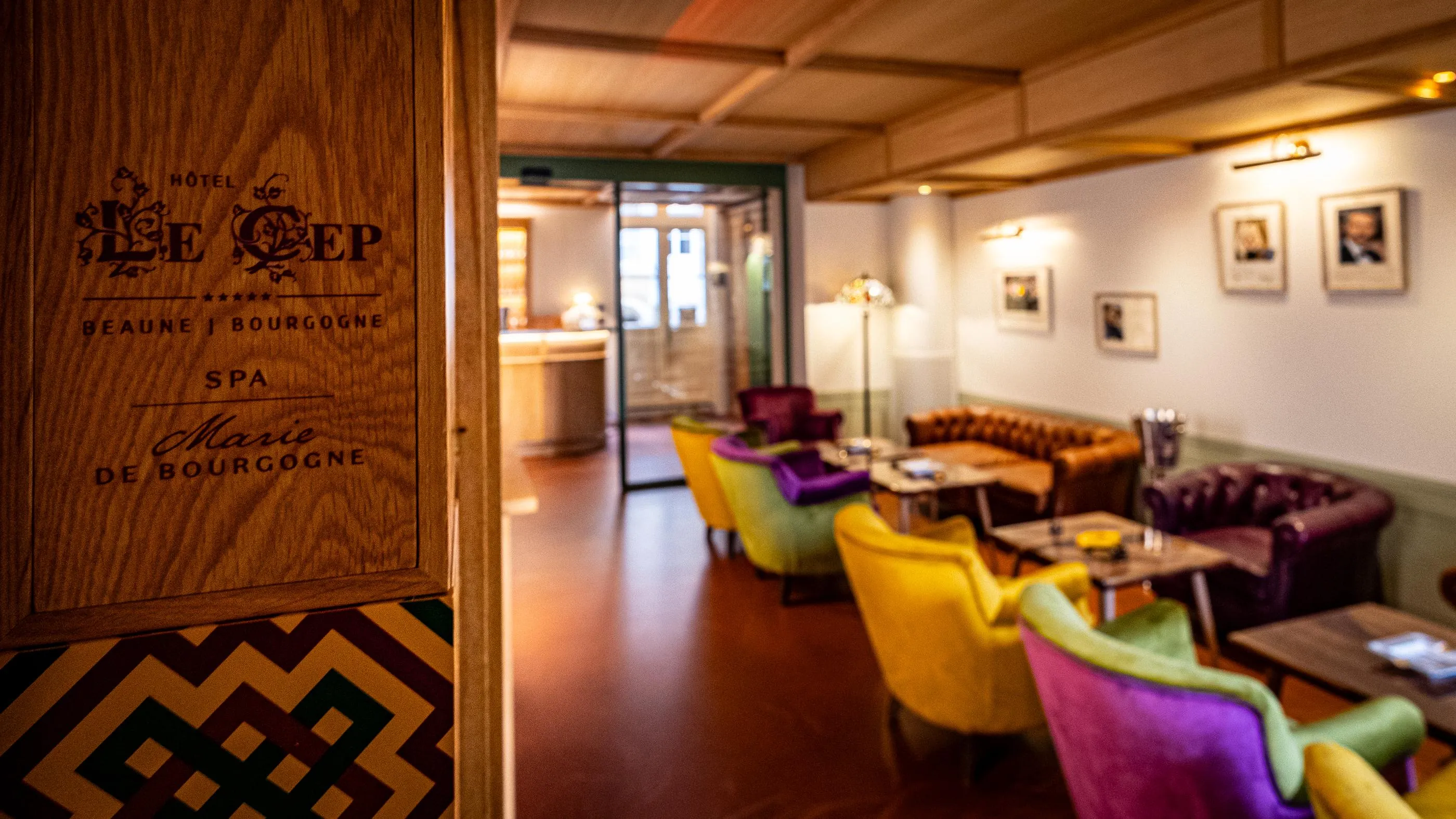 Intérieur d'un hôtel avec des fauteuils colorés et une porte en bois portant l'inscription "Hôtel Le Cep"