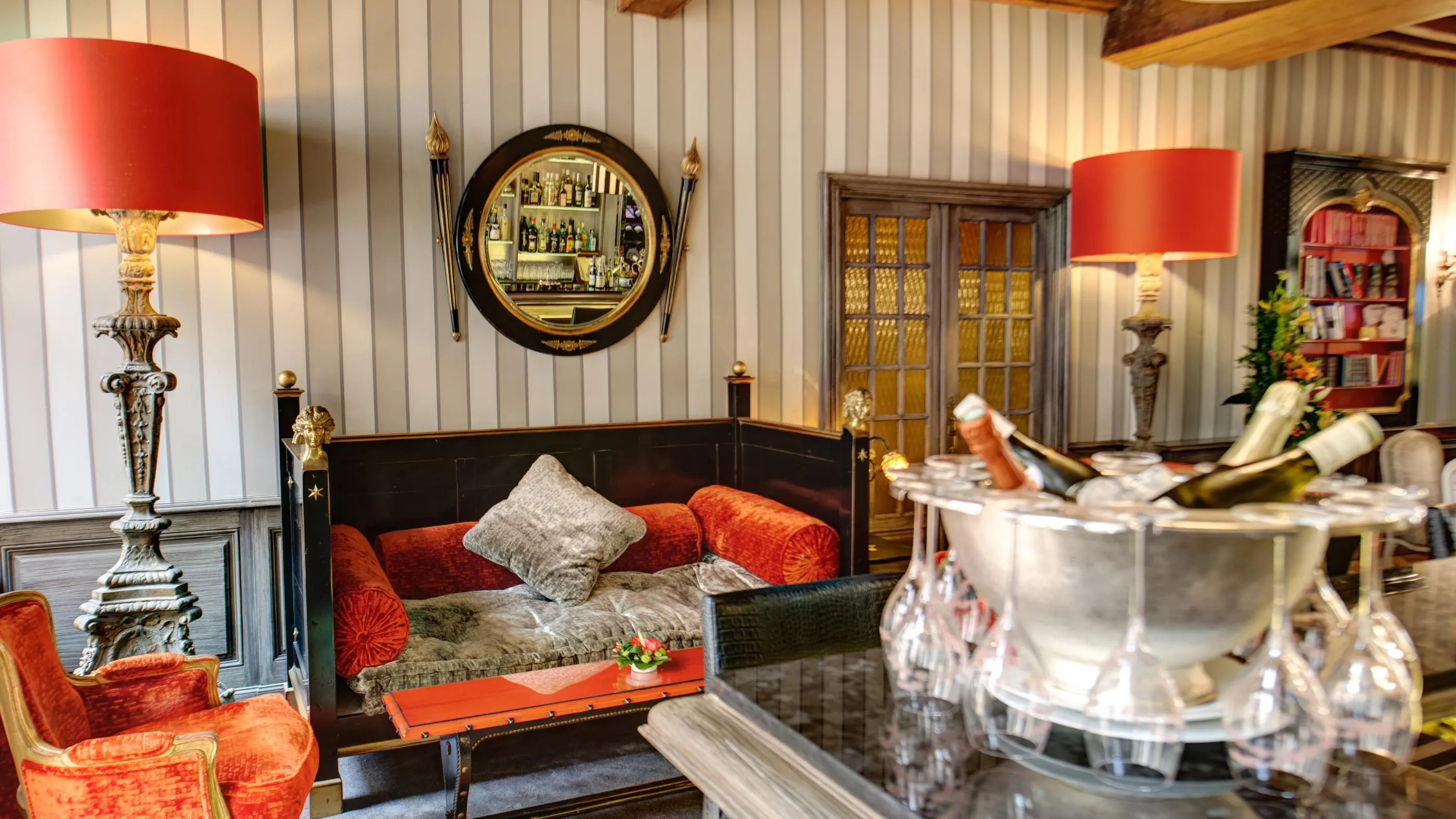 A living room with antique furniture, red lampshades, a round mirror, and shelves filled with books.