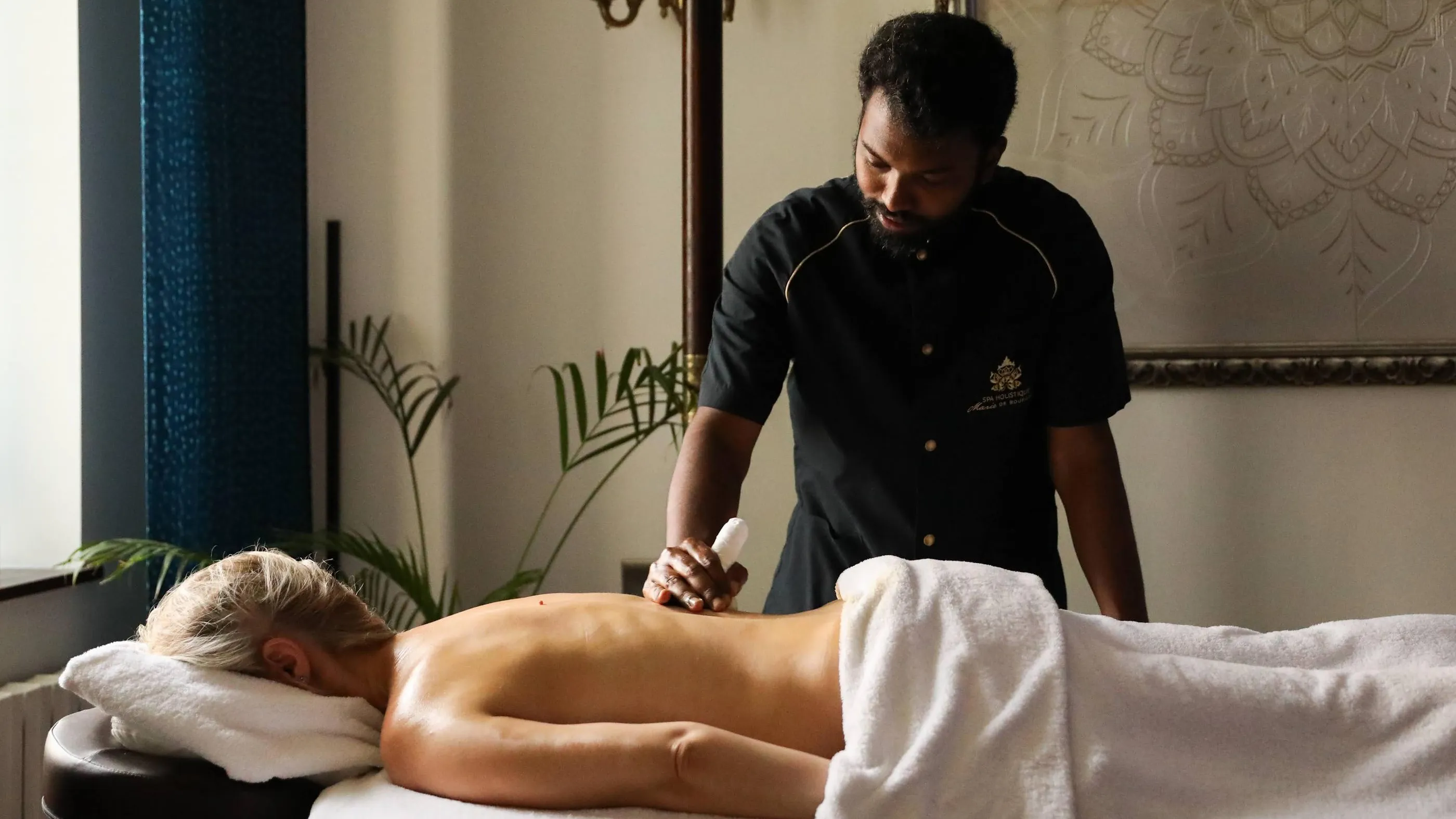 Un professionnel de massage applique un soin sur le dos d'une personne allongée sur une table de massage recouverte de serviettes