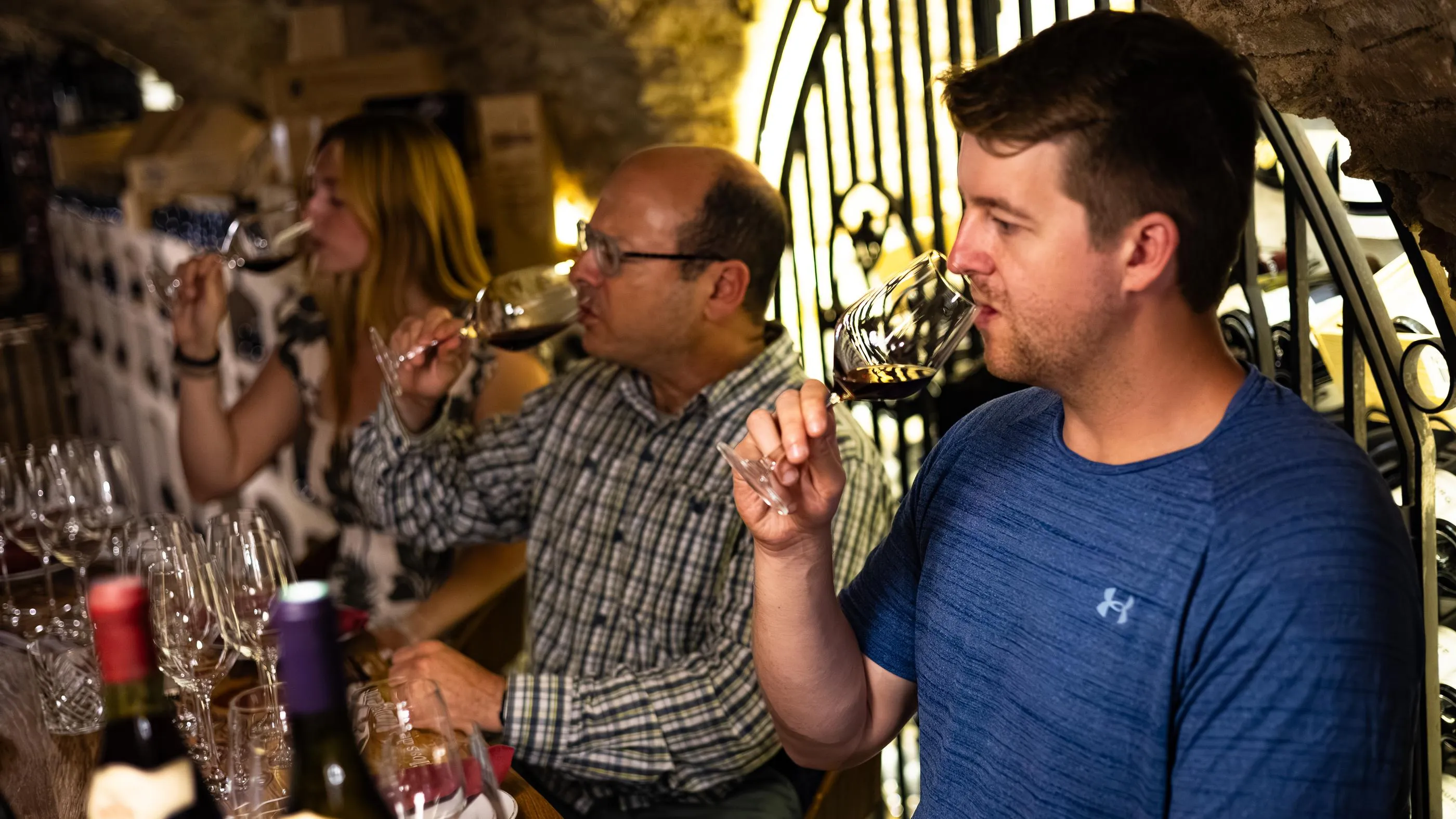 Plusieurs personnes goûtent du vin dans une cave, tenant des verres à vin et des échantillons