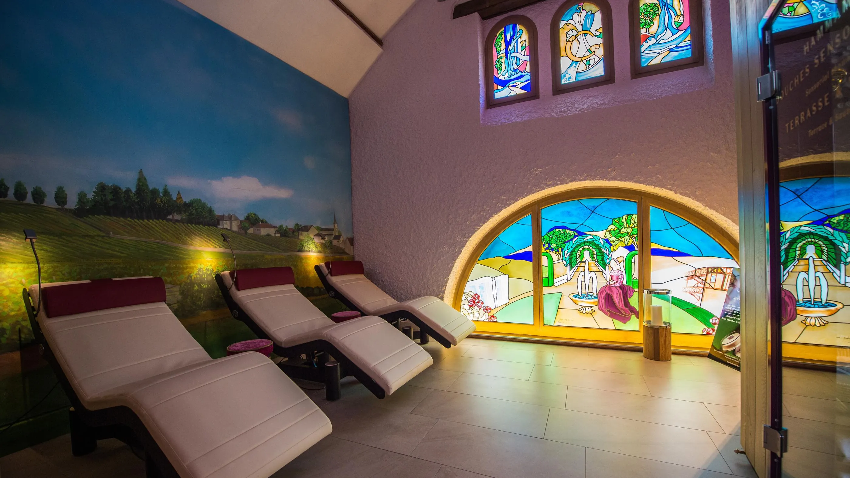 Salle de relaxation avec des lits inclinables et des vitraux colorés représentant des paysages