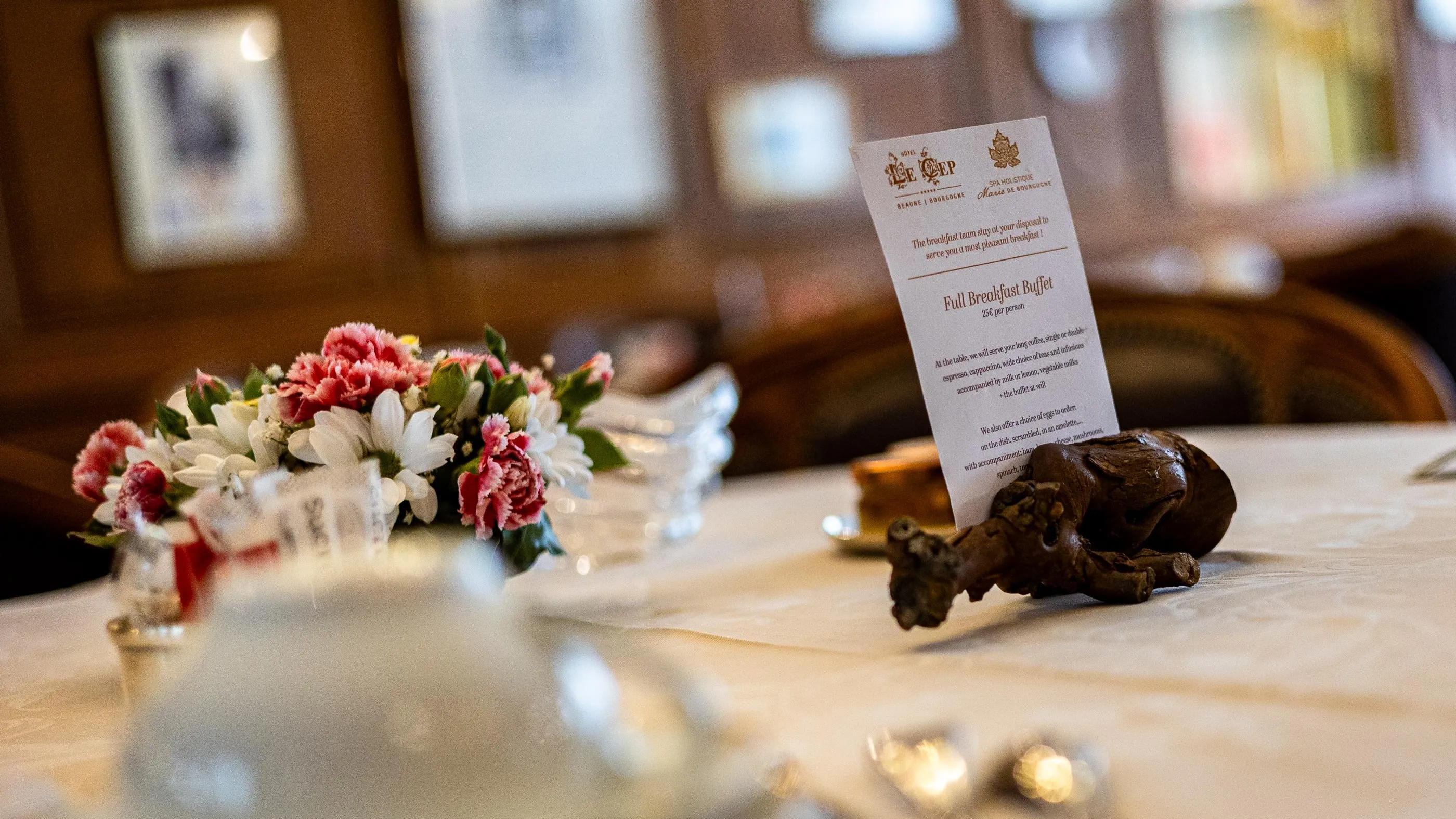 Une carte de menu pour un buffet de petit-déjeuner est posée devant un vase contenant des fleurs roses et blanches sur une table en bois
