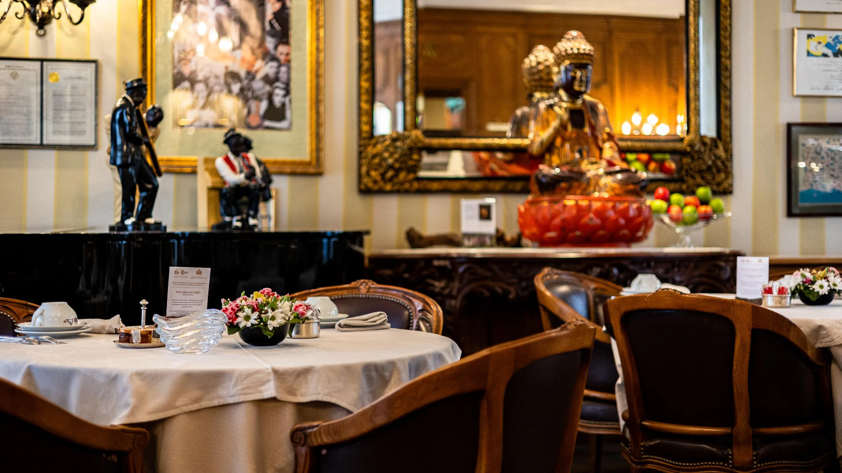 Une salle de restaurant élégante avec des tables dressées, des statues et un miroir orné en arrière-plan