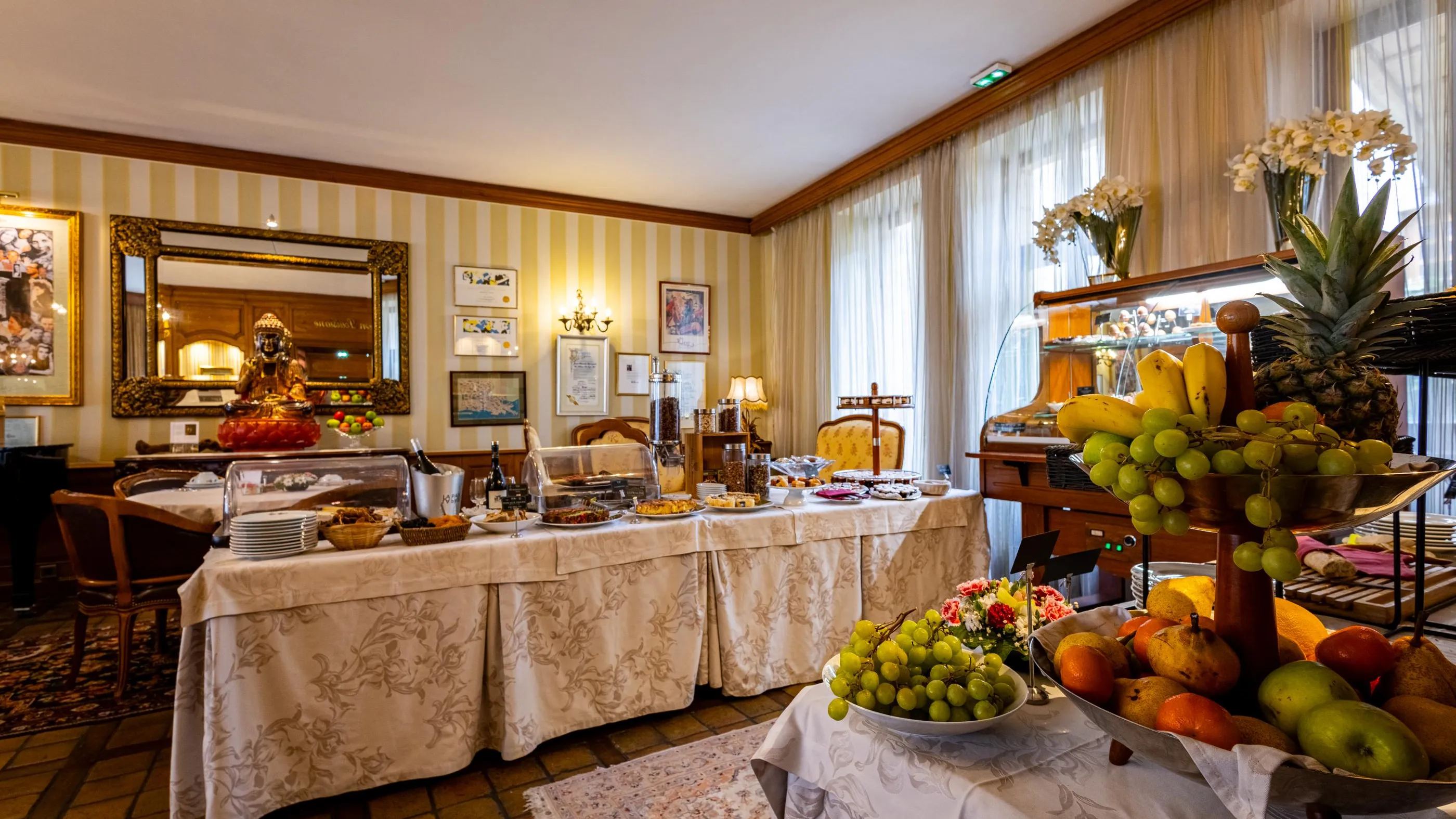 Une salle de petit-déjeuner avec une table garnie de fruits, de boissons et de pâtisseries, des miroirs et des décorations murales