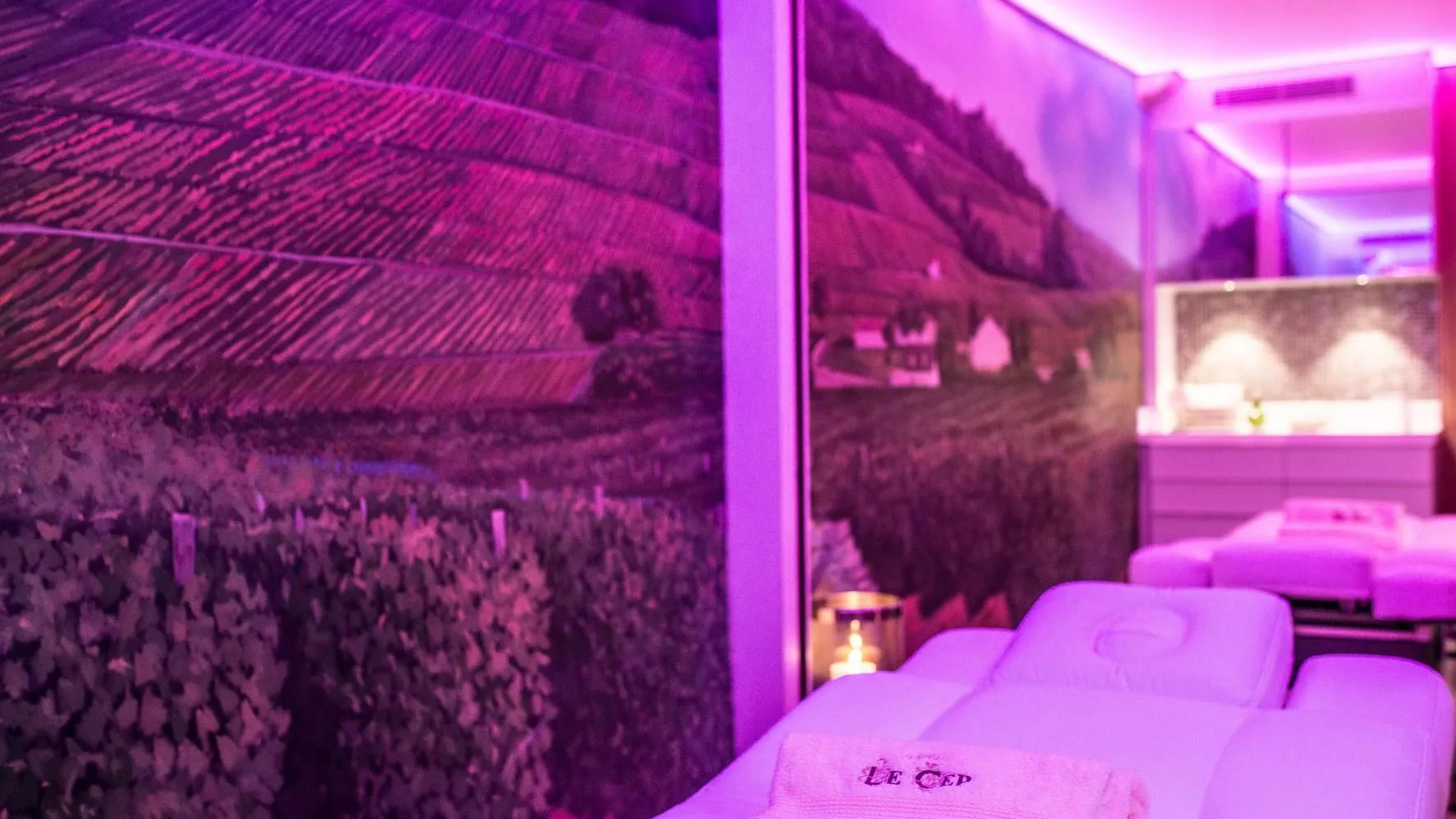Chambre avec des lits et des serviettes, éclairée par une lumière violette, vue à travers une vitre avec des motifs géométriques