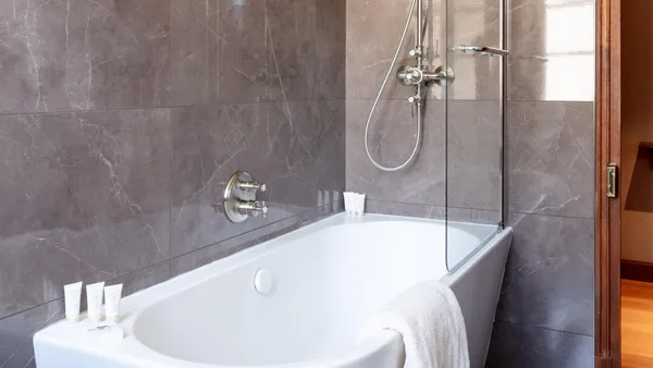 White bathtub with faucet and shower head, surrounded by gray marble tiles and a towel placed on the edge