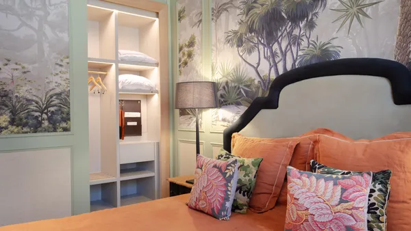 Lit avec une tête de lit grise et noire, des coussins colorés et un mur décoré de motifs de palmiers