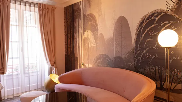 Un salon avec des canapés roses en forme de vagues, une table basse ronde et une grande fenêtre avec des rideaux