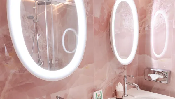 Deux lavabos avec robinetterie argentée, des miroirs ovales éclairés et des accessoires de toilette sur un comptoir en marbre rose