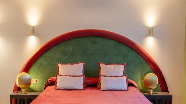 Grande chambre avec un lit à baldaquin rouge et vert, une tête de lit arrondie et deux tables de chevet avec lampes sphériques