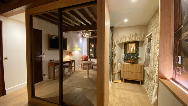 Hall d'entrée avec porte vitrée menant à une salle à manger et une salle de bain, éclairé par des lampes et des spots au plafond
