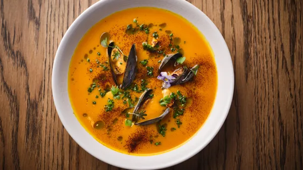 Bowl of orange soup garnished with black cardamom pods, herbs, and spices on a wooden table