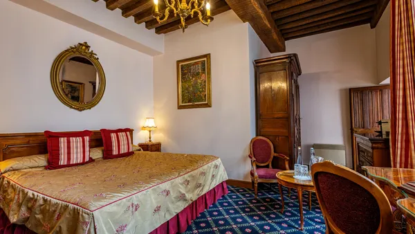 Chambre avec un lit à baldaquin, une table avec deux chaises, un miroir, un tableau et un chandelier au plafond