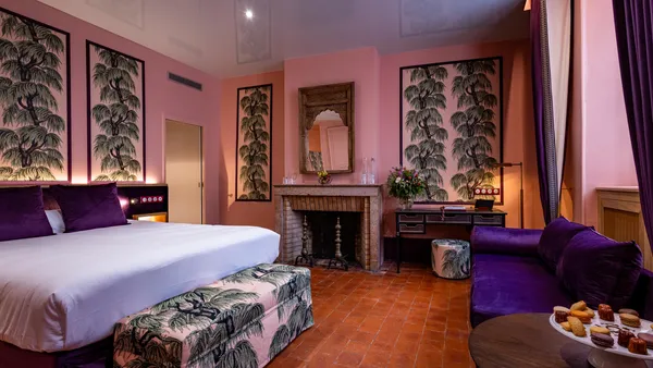 Chambre avec un lit, un canapé, une cheminée et des tableaux aux murs représentant des arbres