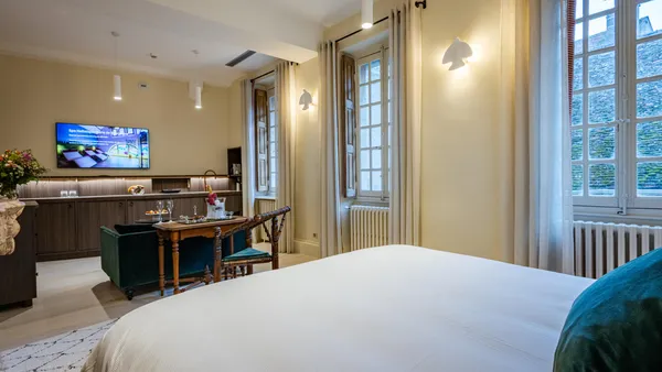Chambre d'hôtel avec lit, bureau, télévision et fenêtres donnant sur un toit en tuiles