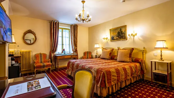 Hotel room with a four-poster bed, two bedside tables, a television, candelabras, and a window with curtains.