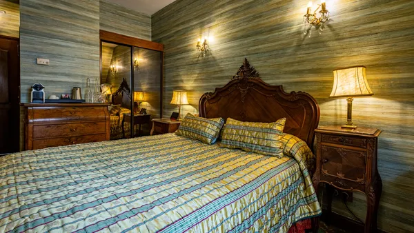 Bedroom with a wooden four-poster bed, a striped blanket, and lit lamps on, against a textured gray-green wall