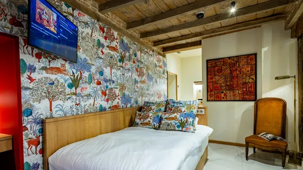 Chambre avec un lit à tête de lit décorée de motifs animaux et végétaux, un fauteuil et un écran mural allumé