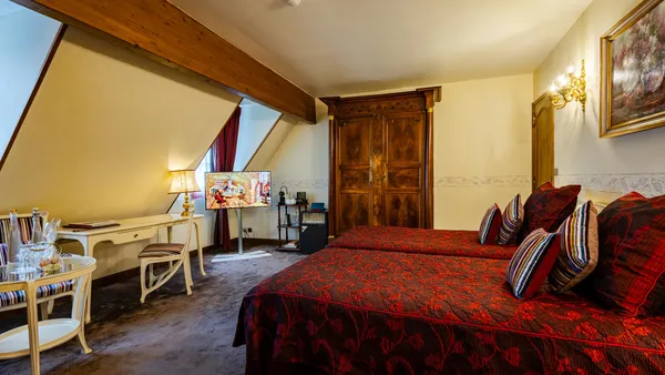 Room with two double beds with red blankets, a bedside table, a desk, and a television.