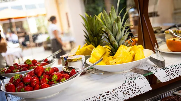 A tray of fruit with strawberries, pieces of pineapple, and a pot of cream, placed on a table covered with a lace tablecloth.