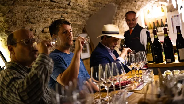 Un groupe de personnes déguste du vin dans un caveau avec des bouteilles et des verres sur une table