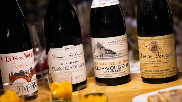 Four bottles of Clos de Vougeot Grand Cru wine placed on a wooden table with yellow flowers