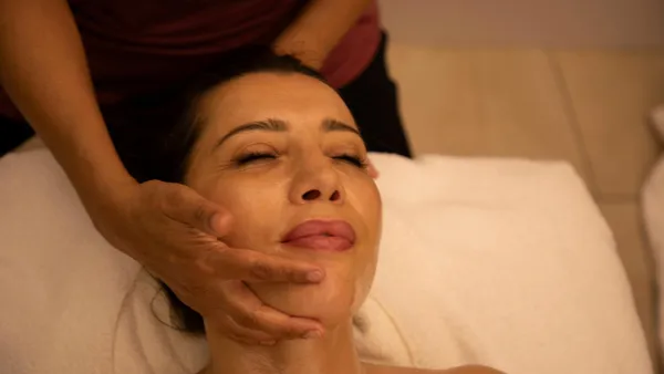 Une personne allongée reçoit un massage du visage par une main visible